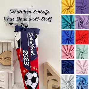 Könnte beinhalten: Ein roter und weißer Schultüte mit einem Fußball-Design. Die Tüte hat ein blaues Band mit dem Text "Schulkind 2023" darauf. Die Tüte ist aus Baumwollstoff und mit Sternen verziert. Das Bild zeigt auch verschiedene Stoffmuster in verschiedenen Farben.