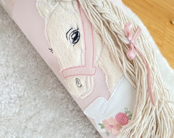 May include: A light pink cone-shaped gift container featuring a plush cream-coloured horse applique with a pink bridle. The horse has a long, braided cream yarn mane adorned with a small pink ribbon bow and a floral embroidery detail at the base.