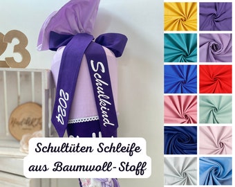 May include: A purple fabric school cone with white text that says "Schulkind" and "2023". The cone is decorated with a purple ribbon and white lace. The text "Schultüten Schleife aus Baumwolle-Stoff" is displayed below the cone.