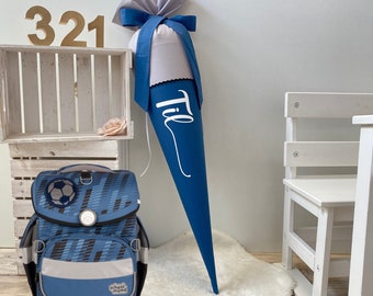 May include: A blue and grey school backpack with a football design. The backpack is next to a blue and white school cone with the name "Til" written on it.