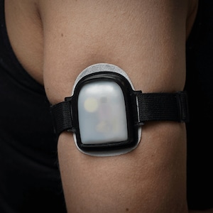 Könnte beinhalten: Ein schwarzes und graues Armband mit einer durchsichtigen Plastikabdeckung über einem kleinen elektronischen Gerät.