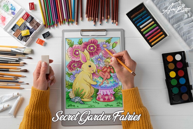 K&ouml;nnte beinhalten: Eine Person koloriert eine detaillierte Illustration einer Fee, die auf einem Pilz sitzt, mit einem Hasen an ihrer Seite. Die Illustration ist von Blumen und Bl&auml;ttern umgeben. Das Bild zeigt auch verschiedene Kunstmaterialien, darunter farbige Bleistifte, Pinsel und Aquarellfarben.