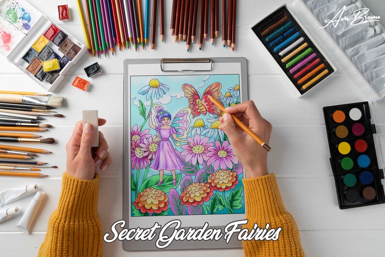 K&ouml;nnte beinhalten: Eine Person malt eine Seite aus einem Malbuch mit Buntstiften aus. Die Seite zeigt eine Fee mit Fl&uuml;geln und Blumen. Der Titel der Seite lautet "Secret Garden Fairies".