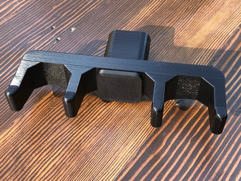 May include: Black plastic 3D printed tool with four prongs and a square base. The tool is designed to hold and secure objects.