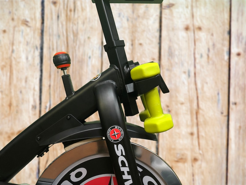 May include: Black exercise bike with a silver wheel and a black and red logo that says "Schwinn". There are two yellow dumbbells attached to the bike.