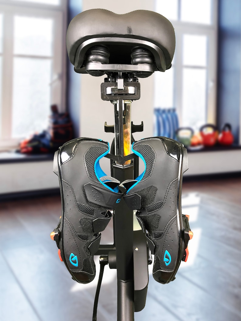 May include: Black cycling shoes with blue accents and a black bike seat attached to a black stand.