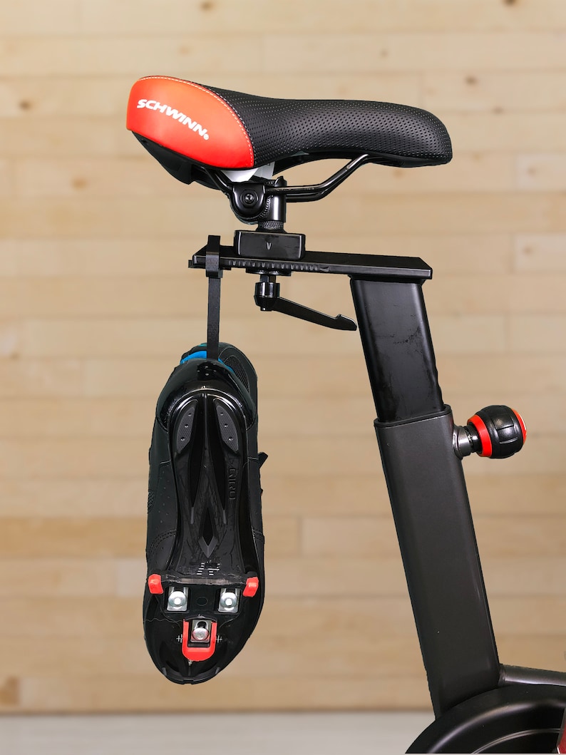 May include: A black exercise bike with a red and black seat that says "SCHWINN" on it. A black cycling shoe with red cleats is hanging from the bike.