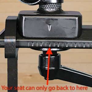 May include: Close-up of a black camera mount with a sliding seat. The seat is at its furthest back position, indicated by a small arrow and the text "Your seat can only go back to here with the shoe holder installed."