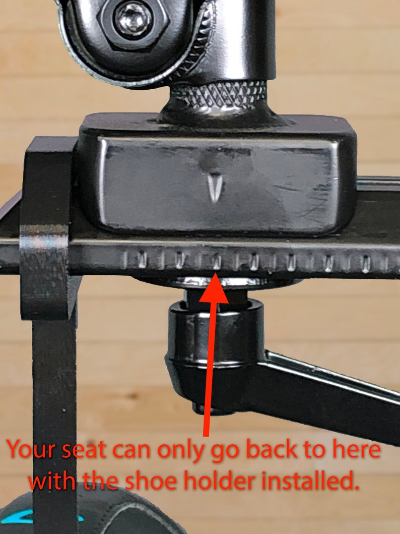 May include: Close-up of a black camera mount with a sliding seat. The seat is at its furthest back position, indicated by a small arrow and the text "Your seat can only go back to here with the shoe holder installed."
