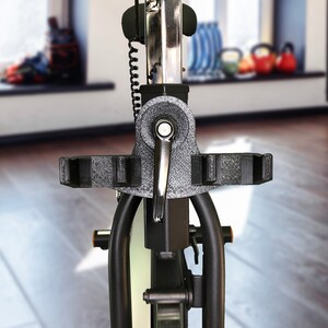 May include: Close-up of a black stationary exercise bike with a silver frame and a black handlebar. The bike is in a gym setting with a window in the background.