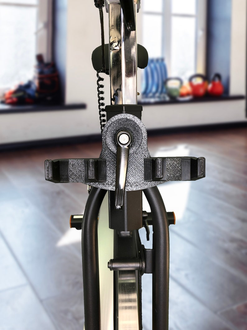 May include: Close-up of a black stationary exercise bike with a silver frame and a black handlebar. The bike is in a gym setting with a window in the background.