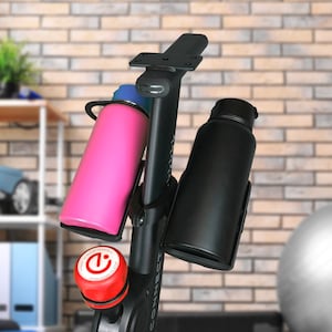 Puede incluir: Bicicleta de ejercicio negra con un porta botellas de agua rosa y negro. La bicicleta tiene un botón rojo que dice "Presiona hacia abajo para detener" y "Conectar" escrito en el lateral.