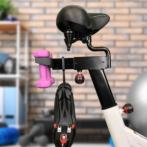 May include: A black exercise bike with a black seat and a white frame. A pair of pink dumbbells and a black cycling shoe are hanging from the bike.