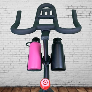 May include: Black exercise bike with a handlebar and two water bottle holders. The holders are filled with a pink and a black water bottle.