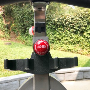 May include: A red button with white text that reads "To Adjust Loosen Then Pull" on a silver exercise bike.