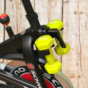 May include: A black exercise bike with a red and white logo that says "Schwinn". The bike has a set of yellow 5 lb dumbbells attached to the handlebars.