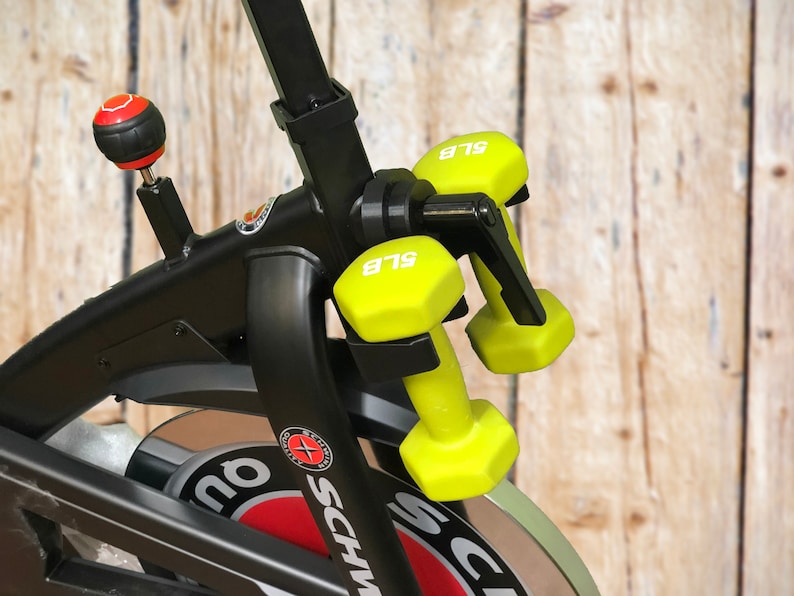May include: A black exercise bike with a red and white logo that says "Schwinn". The bike has a set of yellow 5 lb dumbbells attached to the handlebars.