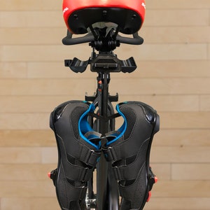 May include: A black indoor cycling bike with a red saddle and black cycling shoes hanging from the handlebars.