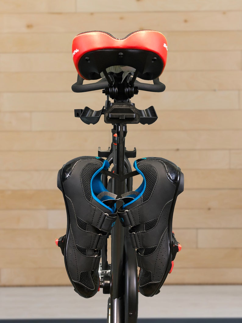 May include: A black indoor cycling bike with a red saddle and black cycling shoes hanging from the handlebars.