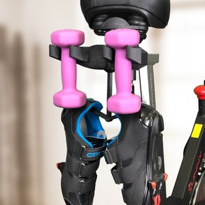 Pu&ograve; includere: Una cyclette nera con una sella nera su cui &egrave; stampata la parola "SUNNY" in rosso. Due manubri rosa sono appesi alla cyclette e un paio di scarpe da ciclismo nere sono appese sotto i manubri.
