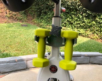 May include: Two lime green dumbbells are attached to a white exercise bike with a black star-shaped knob. The bike has a black and red logo that says "Schwinn Quality".