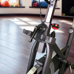 May include: Close-up of a black exercise bike with a silver adjustable seat post and a red knob. The bike has a black frame and a silver wheel.