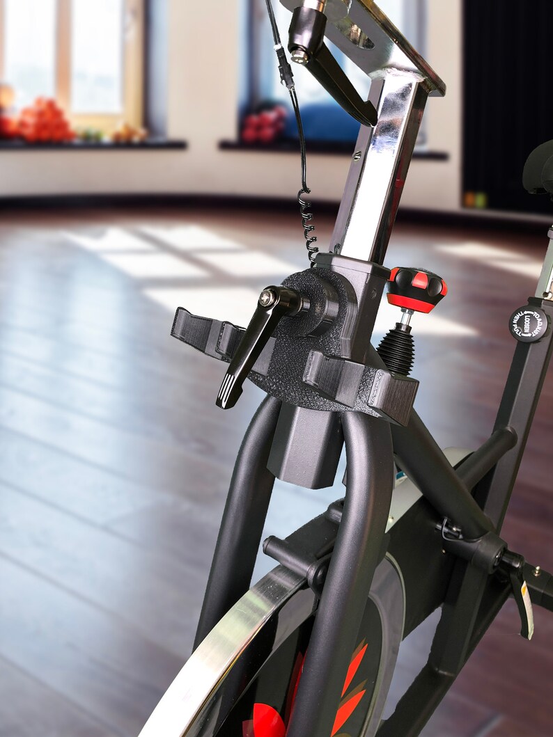 May include: Close-up of a black exercise bike with a silver adjustable seat post and a red knob. The bike has a black frame and a silver wheel.