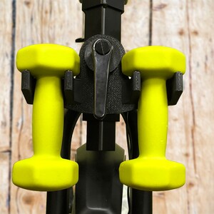 May include: Two yellow dumbbells are attached to a black metal dumbbell rack. The rack has a black lever on the front.