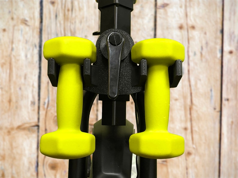 May include: Two yellow dumbbells are attached to a black metal dumbbell rack. The rack has a black lever on the front.