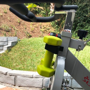 May include: A gray exercise bike with a black water bottle holder and a pair of green dumbbells attached to the handlebars. The bike has a red "Sunny" logo on the side.