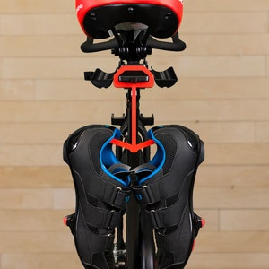 May include: A black and red indoor cycling bike with a black saddle and black cycling shoes hanging on a hook.