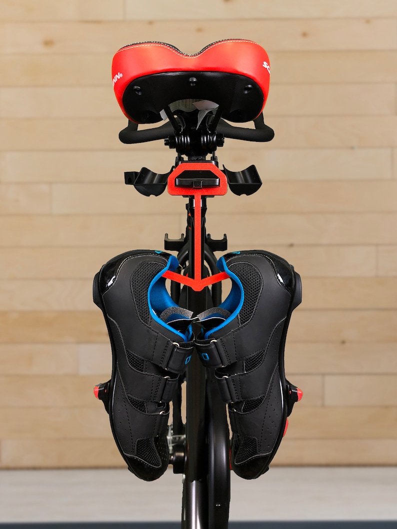 May include: A black and red indoor cycling bike with a black saddle and black cycling shoes hanging on a hook.