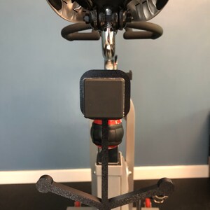 May include: A black metal hook attached to a stationary bike. The hook is shaped like an anchor and has a black foam covering.