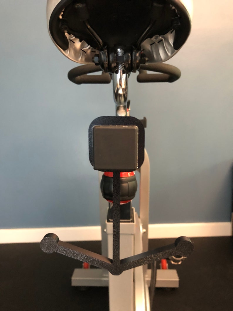 May include: A black metal hook attached to a stationary bike. The hook is shaped like an anchor and has a black foam covering.