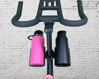 May include: Black stationary bike with a black handlebar and two water bottle holders. A pink water bottle is in the left holder and a black water bottle is in the right holder.