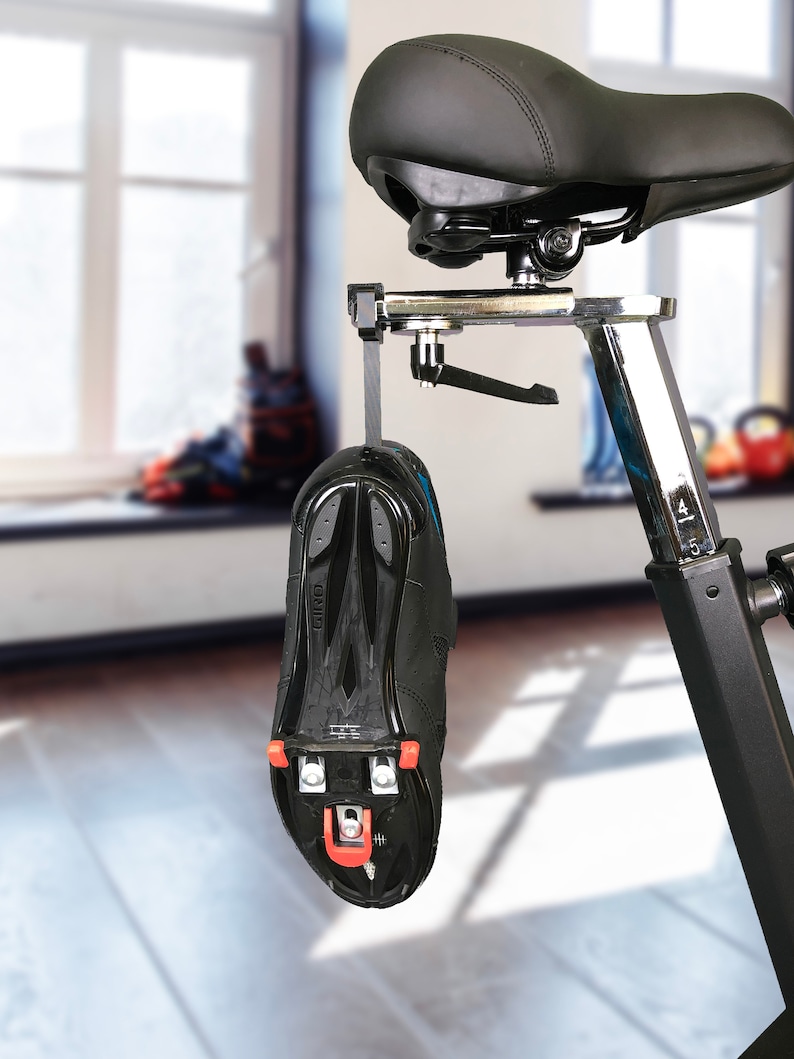 May include: A black stationary bike with a black seat and a black cycling shoe hanging from the frame.