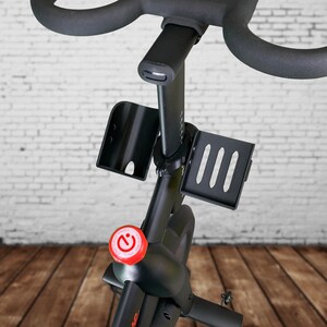 May include: Black stationary bike with a red button labeled "C", a black water bottle holder, and a black phone holder with three slots.