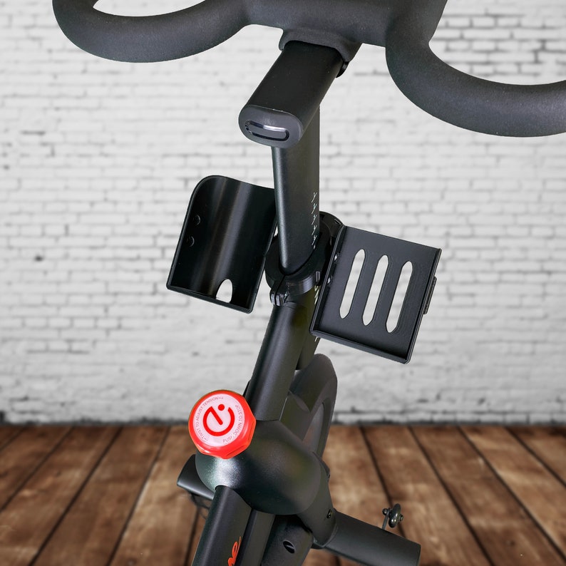 May include: Black stationary bike with a red button labeled "C", a black water bottle holder, and a black phone holder with three slots.