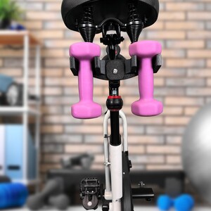 May include: A black exercise bike with a padded seat and a holder for two pink dumbbells attached to the seat post.
