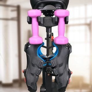 Pu&ograve; includere: Bicicletta da esercizio nera con una sella nera, manubri rosa e scarpe da ciclismo nere appese alla bicicletta. La bicicletta ha un telaio nero e una base argentata. La sella ha la scritta "SUNNY" stampata in rosso.