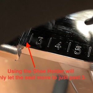 May include: Close-up of a silver metal ruler with numbers 3, 4, 5, and 6 marked on it. An arrow points to the number 3. The text "Using the Shoe Holder will only let the seat move to just past 3." is written below the ruler.