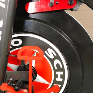 May include: A red anchor-shaped bike stand attached to a black bike wheel with a white sticker that says "Schwinn" on it.
