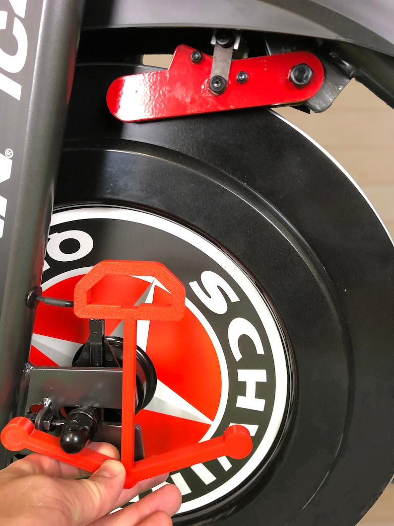 May include: A red anchor-shaped bike stand attached to a black bike wheel with a white sticker that says "Schwinn" on it.