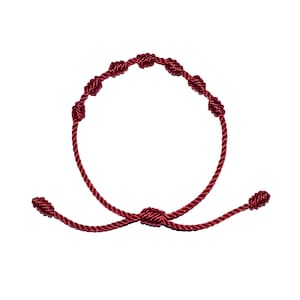 May include: A burgundy-colored knotted bracelet. The bracelet features a series of evenly spaced knots along the circular band, with a larger knot at the center and two smaller knots at the ends. The cord is a deep red color.