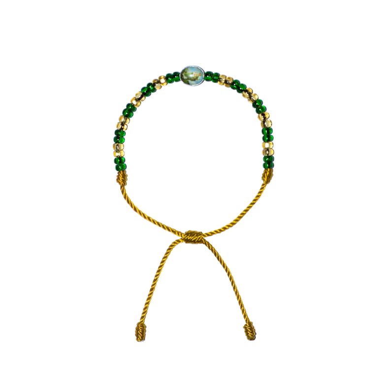 Op de afbeelding: Een groene en gouden kralen armband met een kleine ronde bedel. De armband is vastgebonden met een gouden koord.