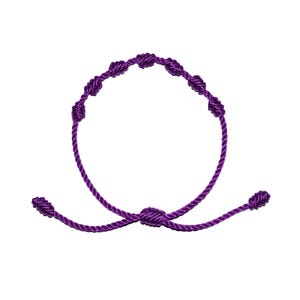 May include: A purple knotted bracelet with an adjustable sliding knot closure. The bracelet features seven evenly spaced knots along the circular band. The cord is a deep shade of purple, creating a simple yet elegant design. The bracelet is shown against a white background.