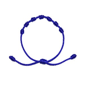 May include: A royal blue knotted bracelet with an adjustable sliding knot closure. The bracelet features seven decorative knots along the circular band. The cord is a solid, vibrant blue color, and the design is simple and elegant.