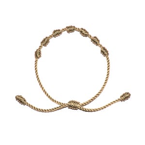 May include: A gold-colored bracelet featuring a series of woven knots. The bracelet has a circular design with a knot closure and adjustable ends. The knots are evenly spaced around the bracelet's circumference.