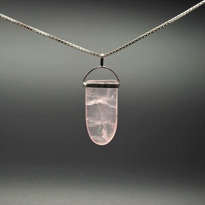 Peut inclure: Un collier en chaîne argent avec un pendentif en quartz rose. Le pendentif a la forme d'une larme et est doté d'une bélière en argent.
