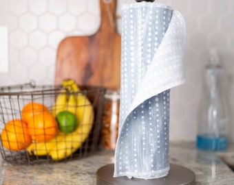 May include: A stainless steel paper towel holder with a roll of blue and white patterned paper towels. The paper towels have a dotted design. A wire basket of fruit and a wooden cutting board are in the background.